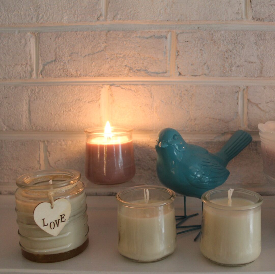 A candle lit in front of two candles and a bird.