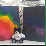 A stuffed bear sitting next to two paintings.