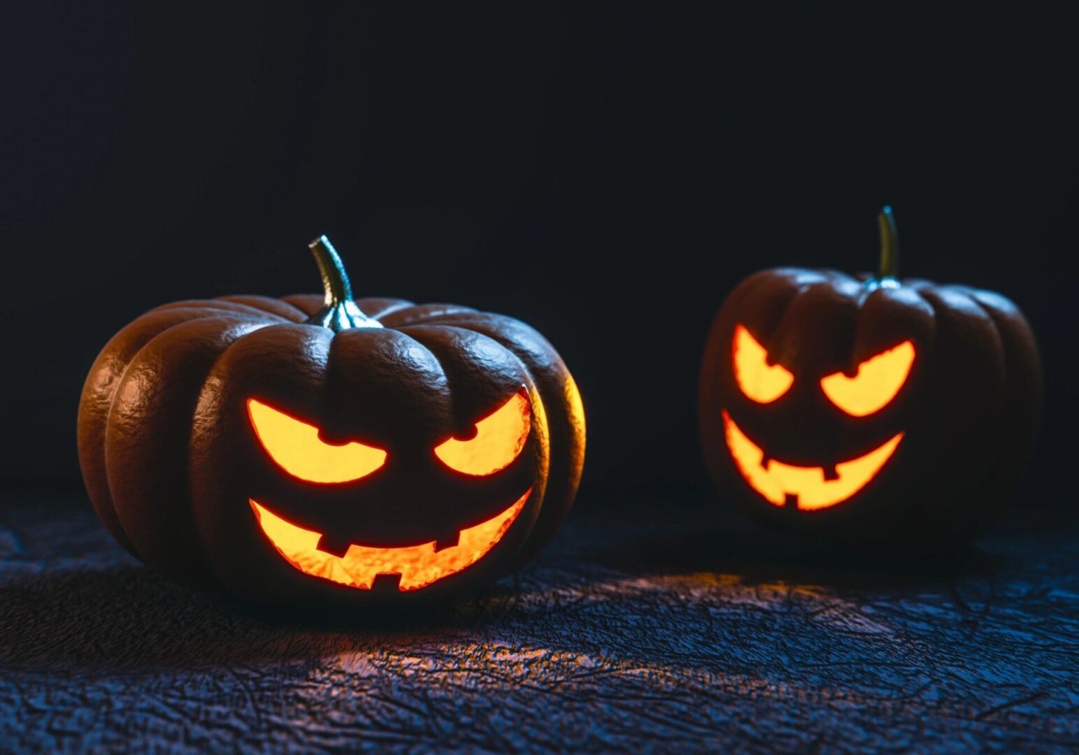 Two lit up pumpkins sitting on a table.